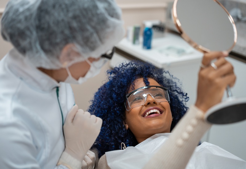 A smiling patient admires the results in a mirror after a cosmetic dental treatment in St. Louis, MO