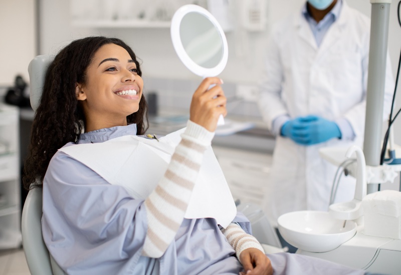 A smiling woman admires the teeth whitening results in a mirror at a dental office in St. Louis, MO